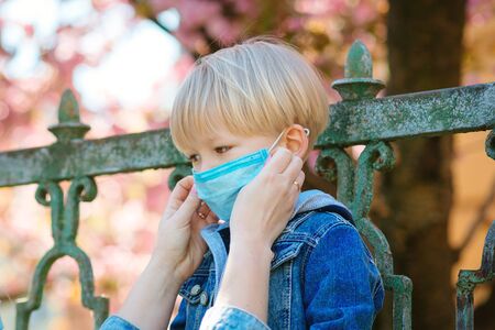 Little boy and mom in medical mask. Mother puts on her baby sterile medical mask. Child, wearing face mask, protect from infection of virus, pandemic, outbreak and epidemic of disease on quarantine.の写真素材