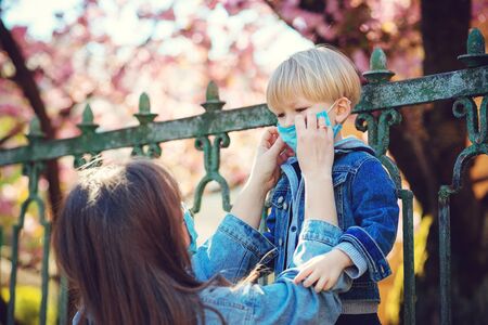 Little boy and mom in medical mask. Mother puts on her baby sterile medical mask. Child, wearing face mask, protect from infection of virus, pandemic, outbreak and epidemic of disease on quarantine.の写真素材
