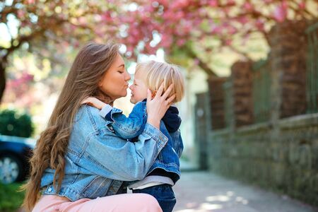 Mother soothing her sad child outdoors. Mom with upset baby on a walk at spring. Toddler boy crying at street. Motherhood, family and lifestyle. Family outdoors. Mother hugging her sad son.の写真素材