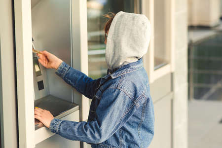 Boy takes money in cash dispenser for alien card. Boy takes cash at ATM machine. Kids theft. Stealing credit card from parents.の素材 [FY310156955690]