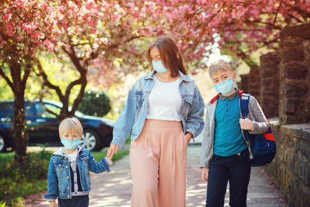 Sad family going home during quarantine. Family wearing face masks. Springtime. Health care concept. Back to school. Education. Real life 2020. Mother and pupil of primary school go hand in hand.の写真素材