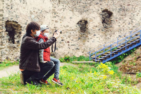 Father teaching his son to take pictures of old castle. Family trip to old castle. Coronavirus quarantine. Parents with son wearing face masks. Happy Father's day. Boy and dad spending time together.の写真素材