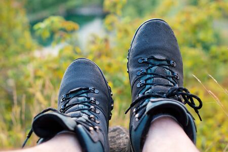 Male legs in hiking boots resting on hillside. Relaxing time during a trekking in a mountains. Beautiful view of mountains. Concept of travelling, hiking and alpinism.の写真素材