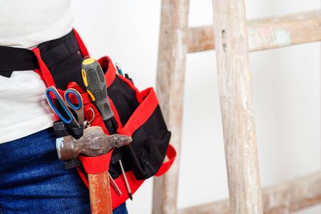 Worker belt with construction tools, closeup. Builder wearing belt with instruments for housework. Isolated on white, copy space. Construction worker with tool belt. House renovation concept.の写真素材