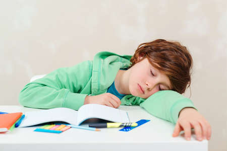 Tired schoolboy sleep at the table during homework. Studying difficulties, education, homework concept. Boy doing homework. Stressed out and tired kid. Frustrated kid sitting at desk with many books.の写真素材