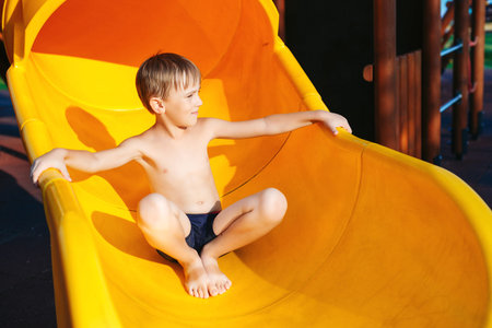 Cute boy having fun at the playground on the beach. Summer vacations. Modern playground at the sea beach. Kid sliding on playground. Summer camp.の写真素材