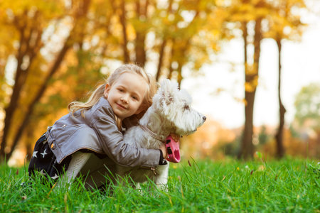 Child girl having fun with her dog during walk in autumn park. Little daughter playing with her west highland white terrier outdoors. Lifestyle portrait. Stylish little girl with pet at nature.の写真素材