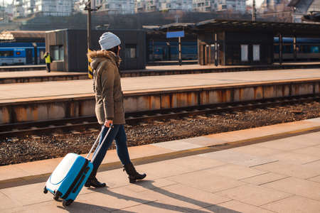 Woman traveller with luggage walkway for travel abroad. Tourist girl walking at railway station. Travel by train. Girl dragging blue luggage suitcase. Journey concept. Lifestyle, travelling, vacation.の写真素材