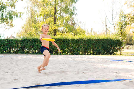 Cute boy playing with flying disk on the beach. Happy kid having fun outdoors in sunny day. Child spending carefree time. Summer vacations with kids. Summer camp.の写真素材