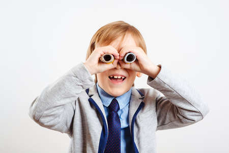 Cute child using money as binoculars. Happy little businessman on white background. Child with binoculars. Financial monitoring of currency. Future profession. Little boss in suit.の写真素材