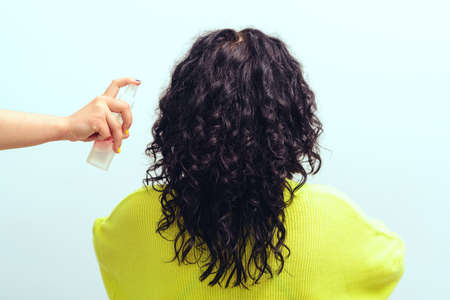Hairstyle with curly hair. Brunette girl with long curly hair, back view. Beautiful woman with wavy hairstyle. Healthy lifestyle, wellness. Woman using spray for styling hair.の写真素材