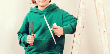 Handsome boy working with spatula. Home renovation. Cute son helps parents to repair room. Kid with tools. New house for family.の写真素材