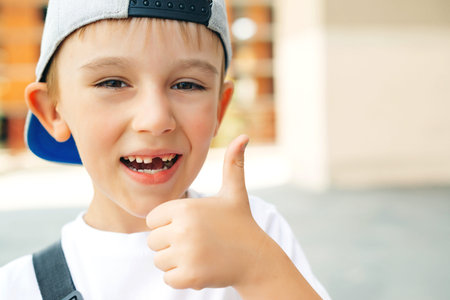 Cute little boy without teeth smiles outdoors. Portrait of fashionable little boy in baseball cap....