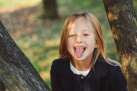 Pretty schoolgirl having fun outdoors. Little girl shows tongue. Happy childhood. Back to school...