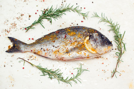 Fresh dorada fish with spices on white board. Healthy food concept. Mediterranean seafood concept. Fish with aromatic herbs and spices. Healthy food, diet or cooking conceptの写真素材