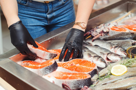 Female hands take salmon steak from showcase. Fish food at shop, close up. Raw fish ready for sale...