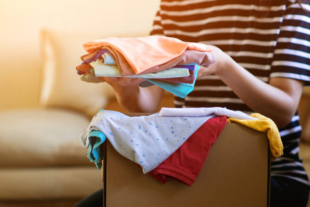 Volunteer with donations for poor people. Cardboard box with clothes for charity. Help poor. Woman...