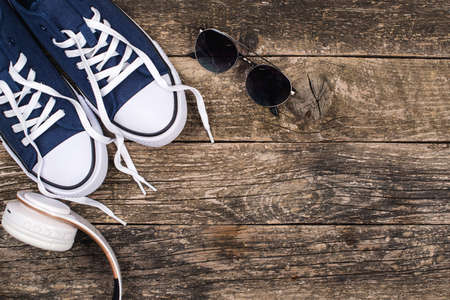 Fashion sneakers, sunglasses and modern wireless headphones. Male fashion. Copy space. Hipster urban style. Headphones and sneakers on wooden rustic background. Set of trendy men accessories, top viewの写真素材
