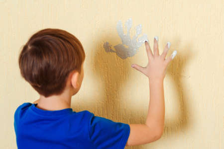 Boy making print of his hand on the wall. Kid painting wall at home. Child having fun during home renovation.の写真素材