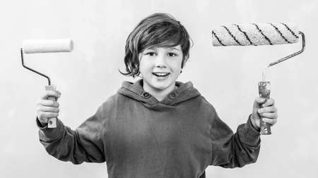 Cute boy with painting roller. Home renovation concept. Son helps parents to paint wall. Boy paints the wall with a roller. The kid holds a brush for painting.の写真素材