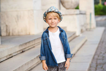 Stylish kid posing outdoors. Cute little boy in summer outfit. Child wearing trendy clothes and hat. Happy child walking in the city street. Happy childhood.の写真素材