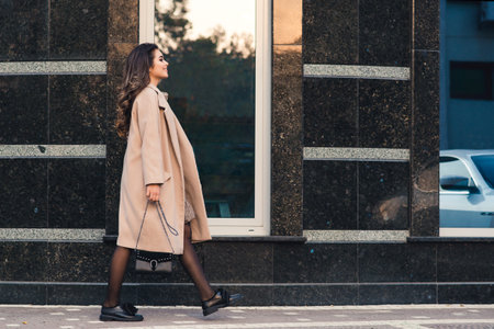 Fashionable woman with long hair walking in the city. Woman wears trendy coat and shoes. Street...
