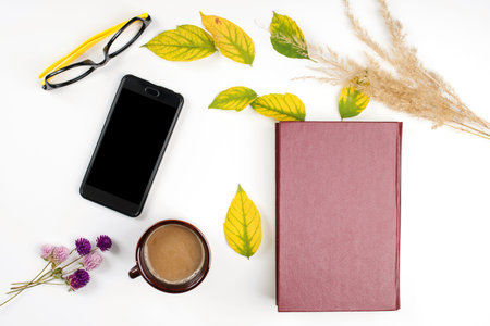 Autumn background with cup of coffee, book, mobile phone and autumn leaves. Mockup with smartphone...