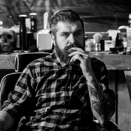 Bearded man sitting in chair at barbershop. Handsome barber man. Barber shop. Bearded hipster with...