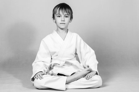 Boy in white kimono practices and meditates. Spirit of martial arts. Little boy sitting in lotus position. Martial arts concept. Healthy sporty childhood and lifestyle.の写真素材