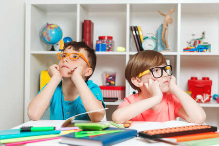 Cute students at workplace in the class. Thoughtful boys sitting at the table. Back to school concept. Boys at lesson in classroom. Smart school kids learning together. Education concept.の写真素材