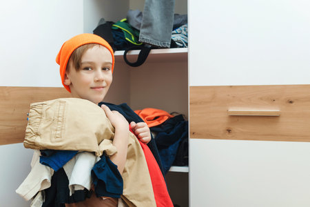 Boy standing near messy clothes on shelf. Preteen boy with dirty clothing in his room. Messy home...