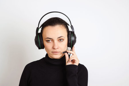 Woman with headphones looking at camera at office. Female call operator is using computer and...