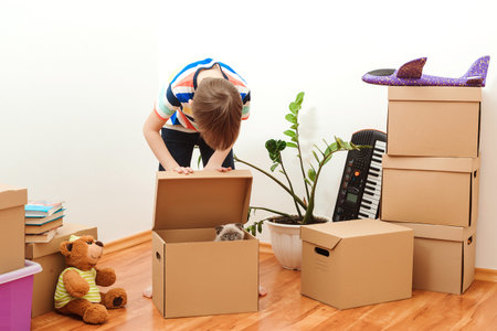 Happy child and cat having fun together at moving day in new home. Housing a young family with kid...