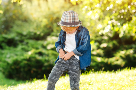 Happy little model posing at summer park. Fashion, lifestyle and summer concept. Happy child walking in sunny day. Handsome kid wearing trendy clothes and summer hat. Kids fashion, lifestyle.の写真素材