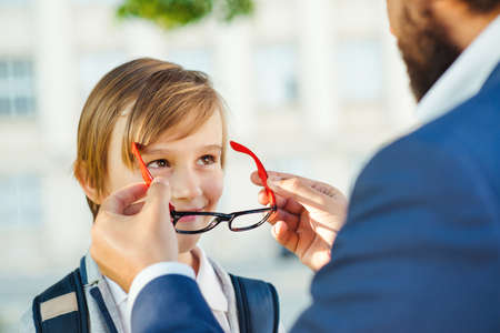 School boy go to first class. Education, elementary school. Father takes child to school. Dad puts on his son glasses. Pupil wearing eyewear. Back to school concept.の写真素材