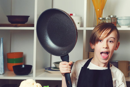 Funny little chef with a pan in kitchen. Boy wearing chef apron. Kid dreaming of future profession....