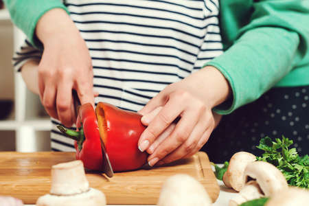Mother teaches her daughter to cutting peper for salad, closeup. Mom and child cooking fresh salad together. Family cooking dinner in kitchen at home.の写真素材