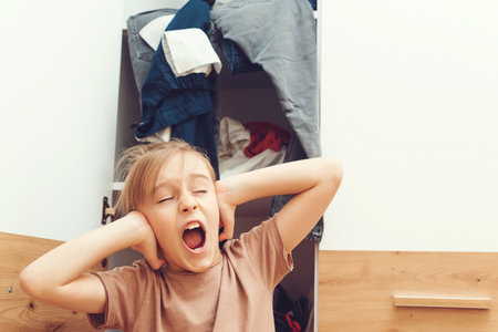 Tired stressed boy cleaning his wardrobe. Mess in wardrobe and dressing room. Nothing to wear concept. Young boy searching clothing in closet. Home chores housework.の写真素材