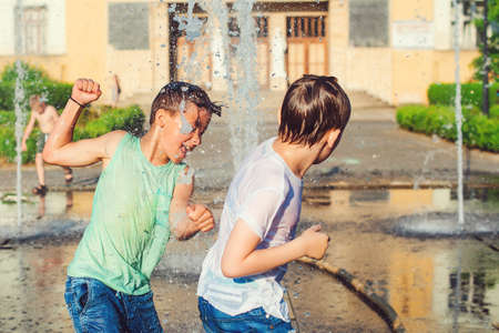 Boys jumping in water fountains. Children playing with a city fountain on hot summer day. Happy friends having fun in fountain. Summer weather. Friendship, lifestyle and vacation.の写真素材