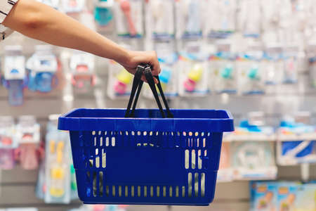 Woman holding shopping basket. Mom is choosing newborn baby product in supermarket. Pregnancy and shopping. Woman choosing baby stuff at baby shop store.の写真素材