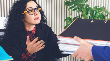 Businesswoman with a lot of work at the workplace. Unfair chief giving assistant papers and...