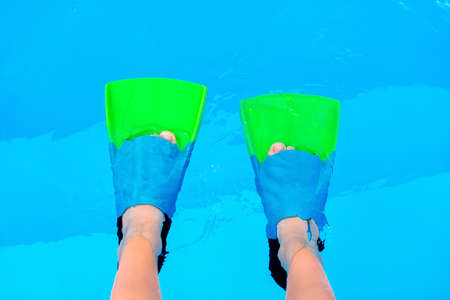 Kid legs with swim flippers over blue water background. Flippers in water. Diver fins. Underwater kids legs in fins in swimming pool, top view. Mockup with copy space.の写真素材
