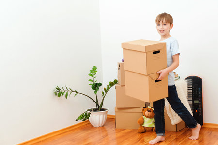 Happy child carrying boxes into new home. Moving day. Happy boy having fun in moving day. Housing a...
