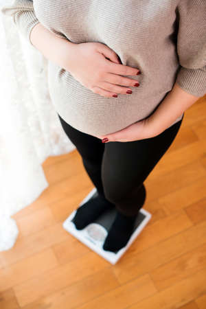 Pregnant woman weighing herself. Woman standing on weight scales at home. Pregnant woman checking her weight. Healthcare, healthy pregnancy and wellness.の写真素材
