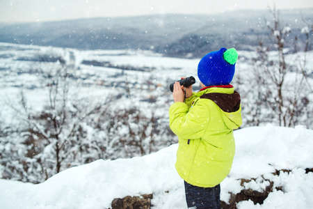 Traveler looking into the distance through binoculars. Travel, childhood and lifestyle concept. Winter expedition vacations outdoor. Happy kid at winter nature.の写真素材