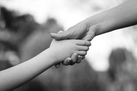 Mother and child hands on nature background. Family support, help and trust. Parent holds the hand of a child on a walk. Kid and mother hands, closeup. Love, relationship and teamwork in family.の写真素材