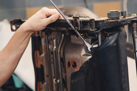 Repair of the old car seat. Car mechanic's hands is using tools. Working hands of a man at the car service, close up.の写真素材