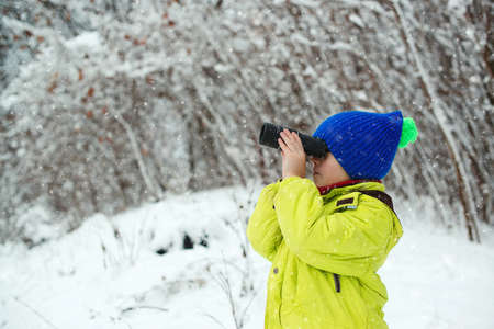 Happy child walking at winter forest. Cute child explorer in snowy forest. Kid looking to monocular. Family winter holidays. Winter fun at nature. Family vacation, snowy day and happy childhood.の写真素材