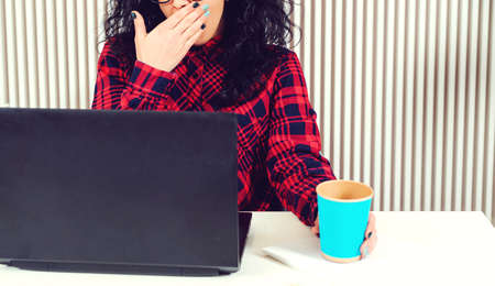 Tired woman yawning at workplace. People, job, career and overwork concept. Sad busy office woman working at laptop computer in the office. Overworked businesswoman.の写真素材