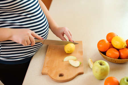 Young pregnant woman preparing fruit salad at home kitchen. Healthy nutrition and diet during pregnancy. Pregnant woman with healthy food.の写真素材
